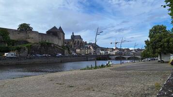 A riverside view with a historic building, a bridge, and a paved walkway.