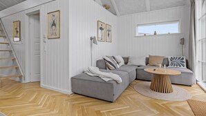 Una sala moderna con un sofá gris, una mesa redonda de centro y un suelo de madera con estampado de espiga.