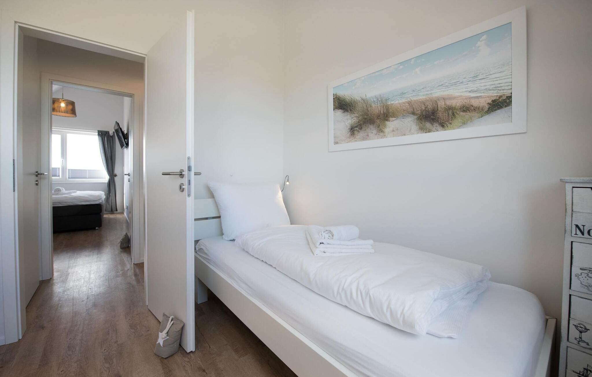 Une chambre avec un lit simple, un tableau représentant une scène de plage et un plancher en bois.