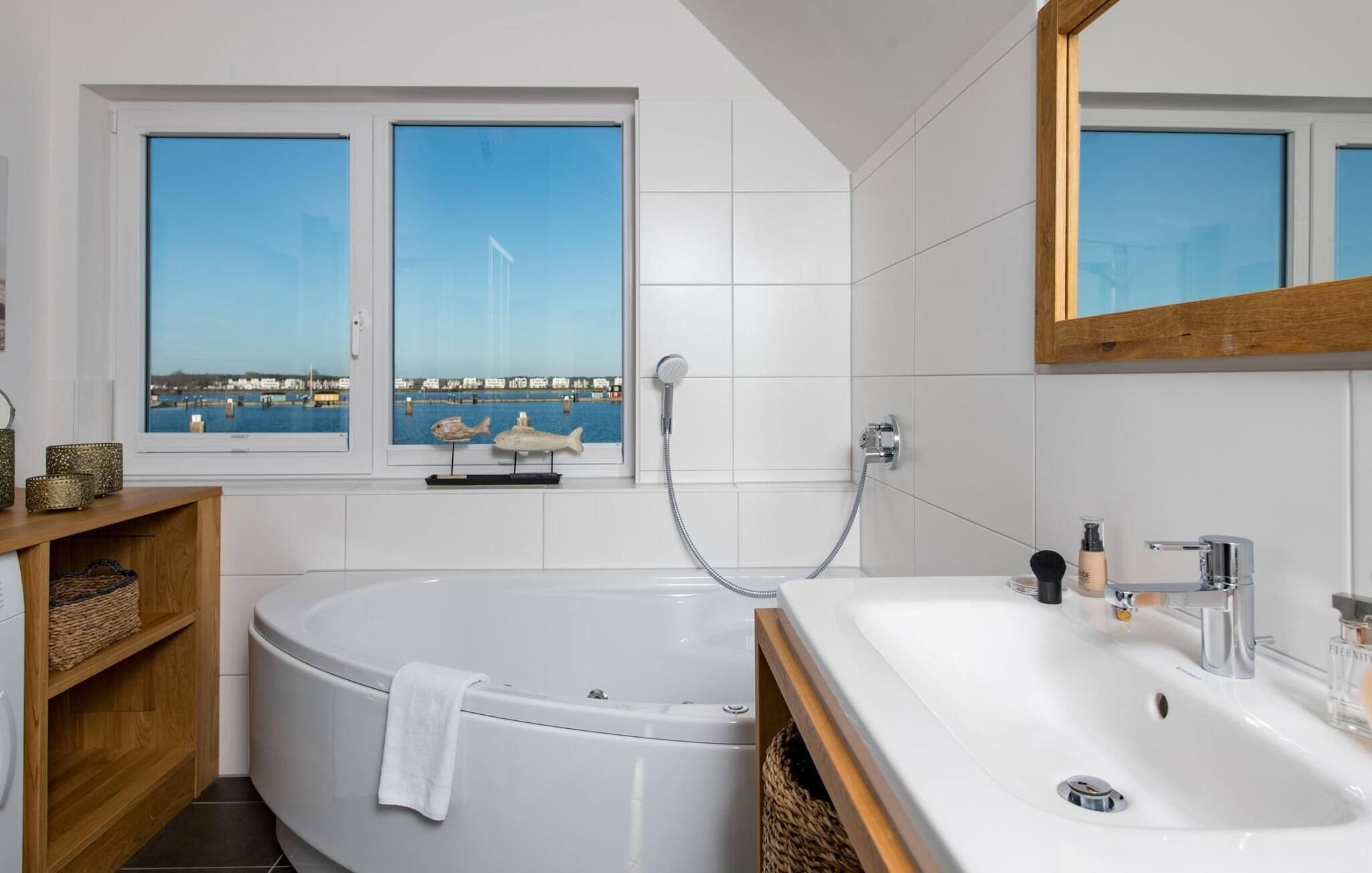A modern bathroom with a bathtub, a sink, and a window with a view of a harbor.