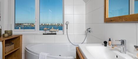 A modern bathroom with a bathtub, a sink, and a window with a view of a harbor.