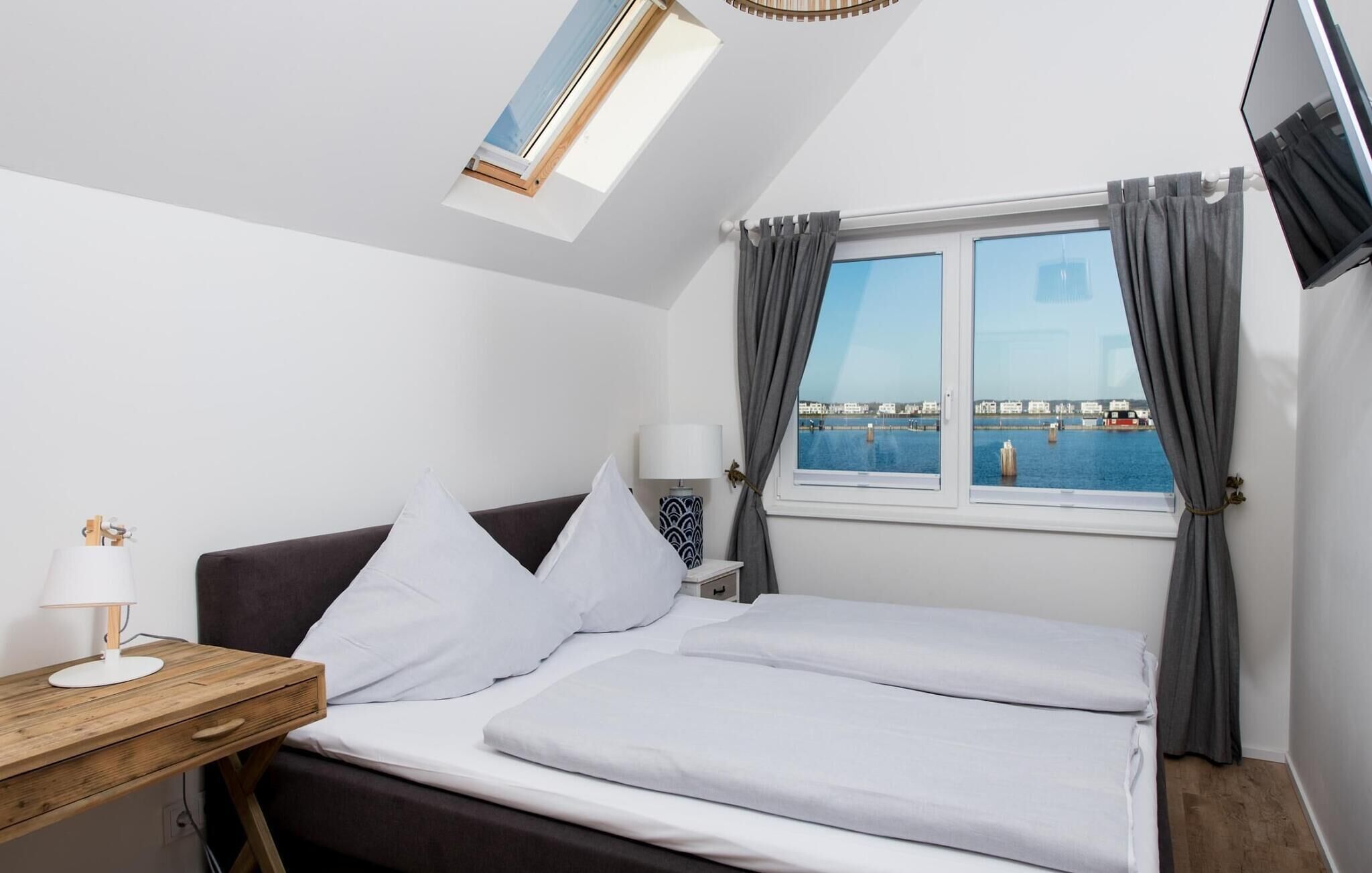 Un dormitorio con cama, escritorio, lámpara y vista al mar a través de una ventana.