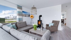 A modern living room with a grey sofa, a coffee table, a fireplace, and a view of the outside. - Cozy home in Olpenitz with sauna (Olpenitz)