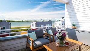 A balcony with a view of a lake, a wooden table with a vase of flowers, and two grey cushioned chairs. - Cozy home in Olpenitz with sauna (Olpenitz)