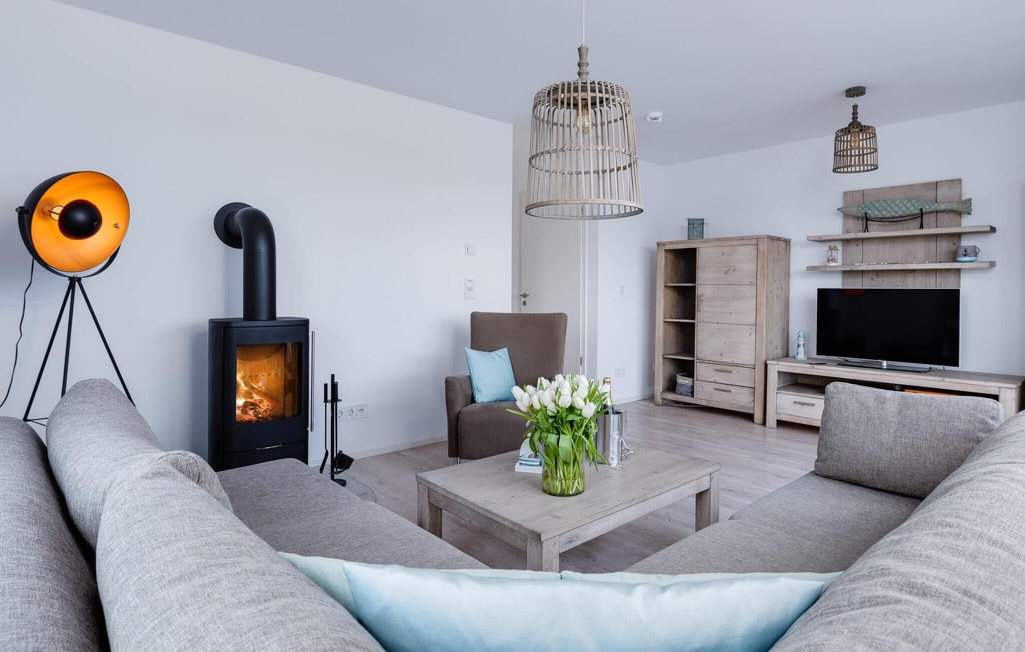 A modern living room with a wood-burning stove, a sofa, a coffee table, a TV, and a hanging light fixture.