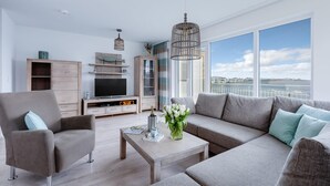 A modern living room with a large window, a television, a sofa, and a coffee table. - Cozy home in Olpenitz with sauna (Olpenitz)