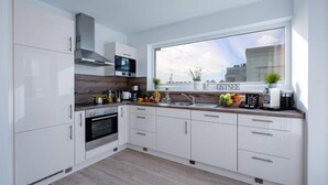 A modern kitchen with white cabinets, a built-in oven, a microwave, and a large window with a city view. - Cozy home in Olpenitz with sauna (Olpenitz)