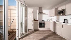 Eine moderne Küche mit weißen Schränken, einem Edelstahlbackofen, einer Mikrowelle und einer Glastür zu einem Außenbereich.