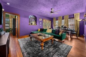 Ein violett gestrichener Raum mit einem grünen Sofa, einem Holztisch und einem Essbereich mit Stühlen und Tisch.