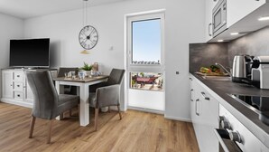 Et moderne køkken med indbygget ovn, mikroovn og kaffemaskine. Der er et spiseområde med et bord og stole, samt et stort vindue med udsigt over byen.