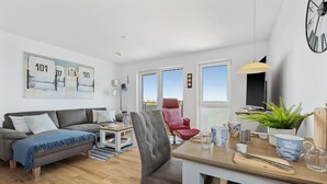 En moderne stue med sofa, lænestol, spisebord og en balkon med en rød stol.