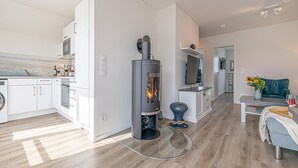 Moderni keittiö, jossa on valkoiset kaapit, sisäänrakennettu uuni ja keskeisellä paikalla sijaitseva puukamiina.