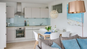 A modern kitchen with white cabinets, a stainless steel range hood, and a dining area with a white table and chairs. - Lovely apartment in Olpenitz with sauna (Olpenitz)