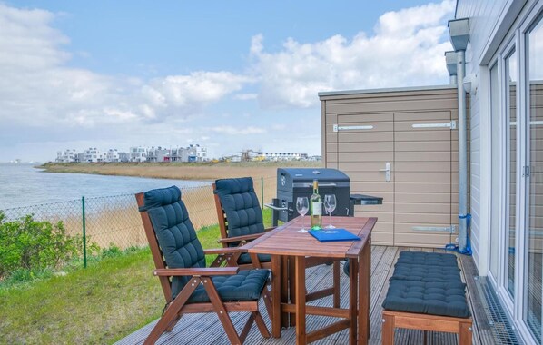 A deck with two chairs and a table, a barbecue grill, and a view of the sea and buildings in the background. - Lovely apartment in Olpenitz with sauna (Olpenitz)