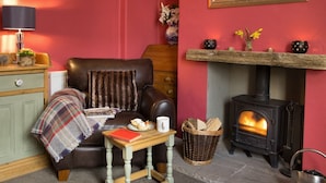 A cozy living room with a fireplace, a leather sofa, a small table with a mug, and a bookshelf.