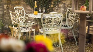 A table set with white metal chairs, a bottle of champagne, and two glasses.