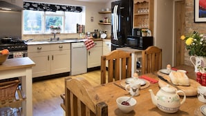 A modern kitchen with a dining area, featuring a refrigerator, stove, and wooden dining table with chairs.