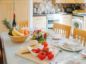 A kitchen with wooden cabinets, a dining table set with plates, glasses, and a fruit bowl.