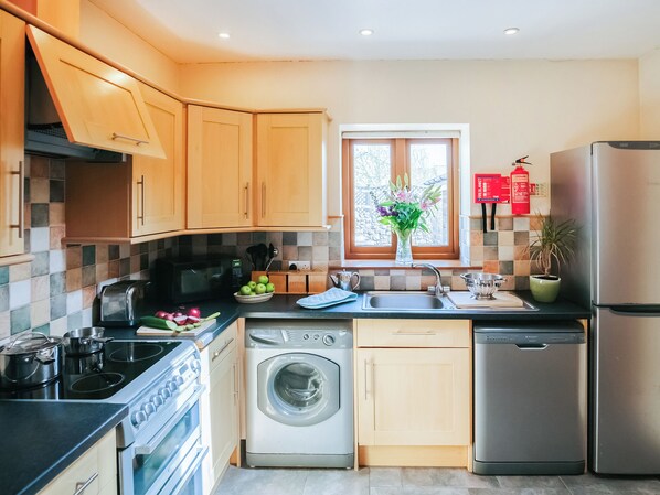 A modern kitchen with wooden cabinets, a built-in oven, a dishwasher, and a refrigerator. - 2 bedroom accommodation in Gower (Gower)