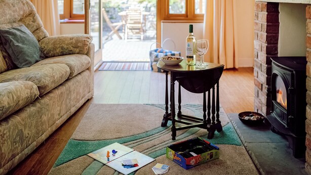 A cozy living room with a sofa, a table with a bottle and glass, a fireplace, and a view through large windows. - 2 bedroom accommodation in Gower (Gower)