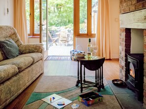 Un salon chaleureux avec un canapé, une table sur laquelle se trouvent une bouteille et un verre, une cheminée et une vue dégagée grâce à de grandes fenêtres.