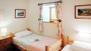 A bedroom with two single beds, a bedside table with a lamp, a window with curtains, and framed pictures on the walls. - 2 bedroom accommodation in Gower (Gower)