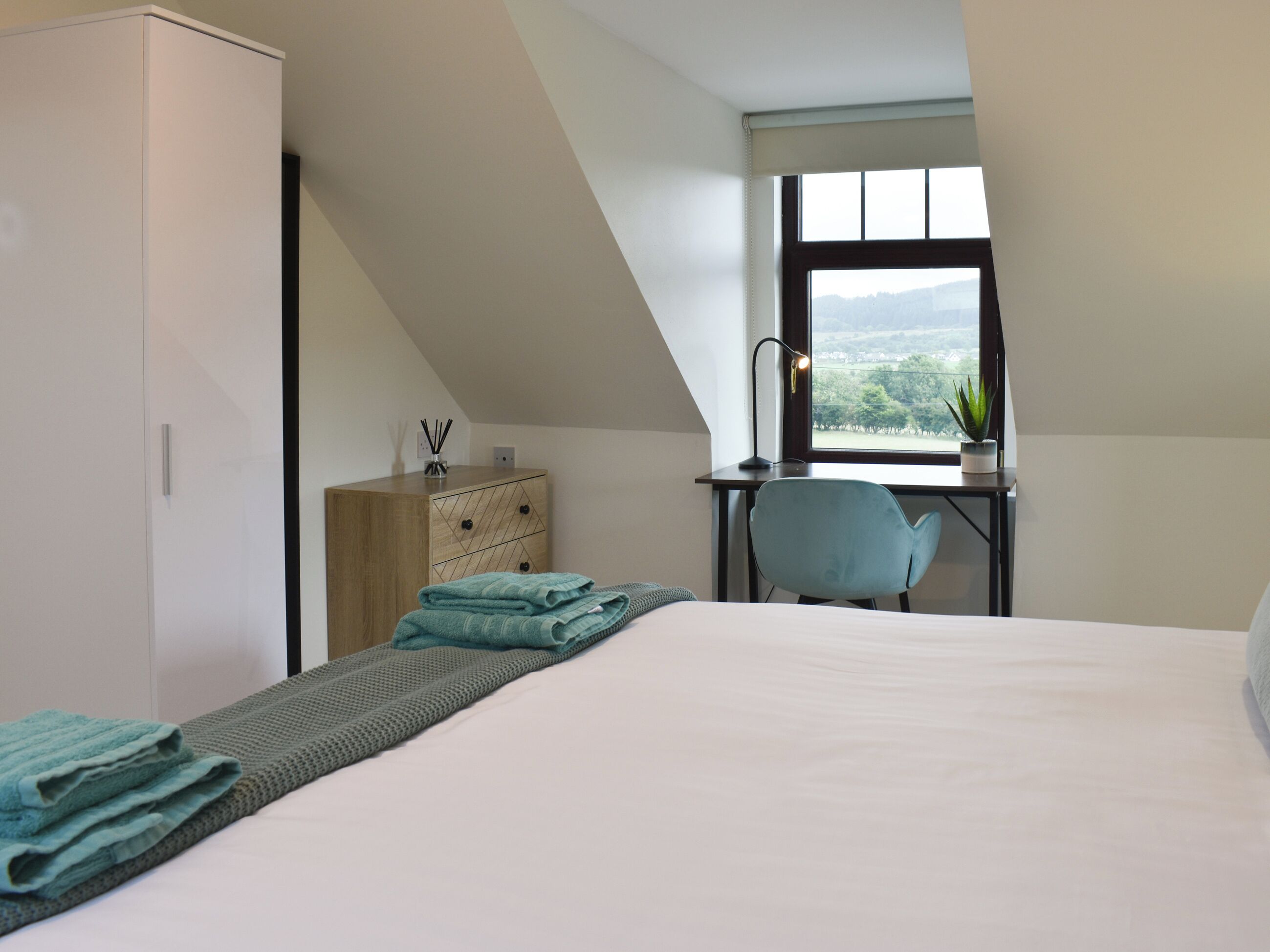 Un dormitorio con cama, escritorio, silla y ventana con vistas.