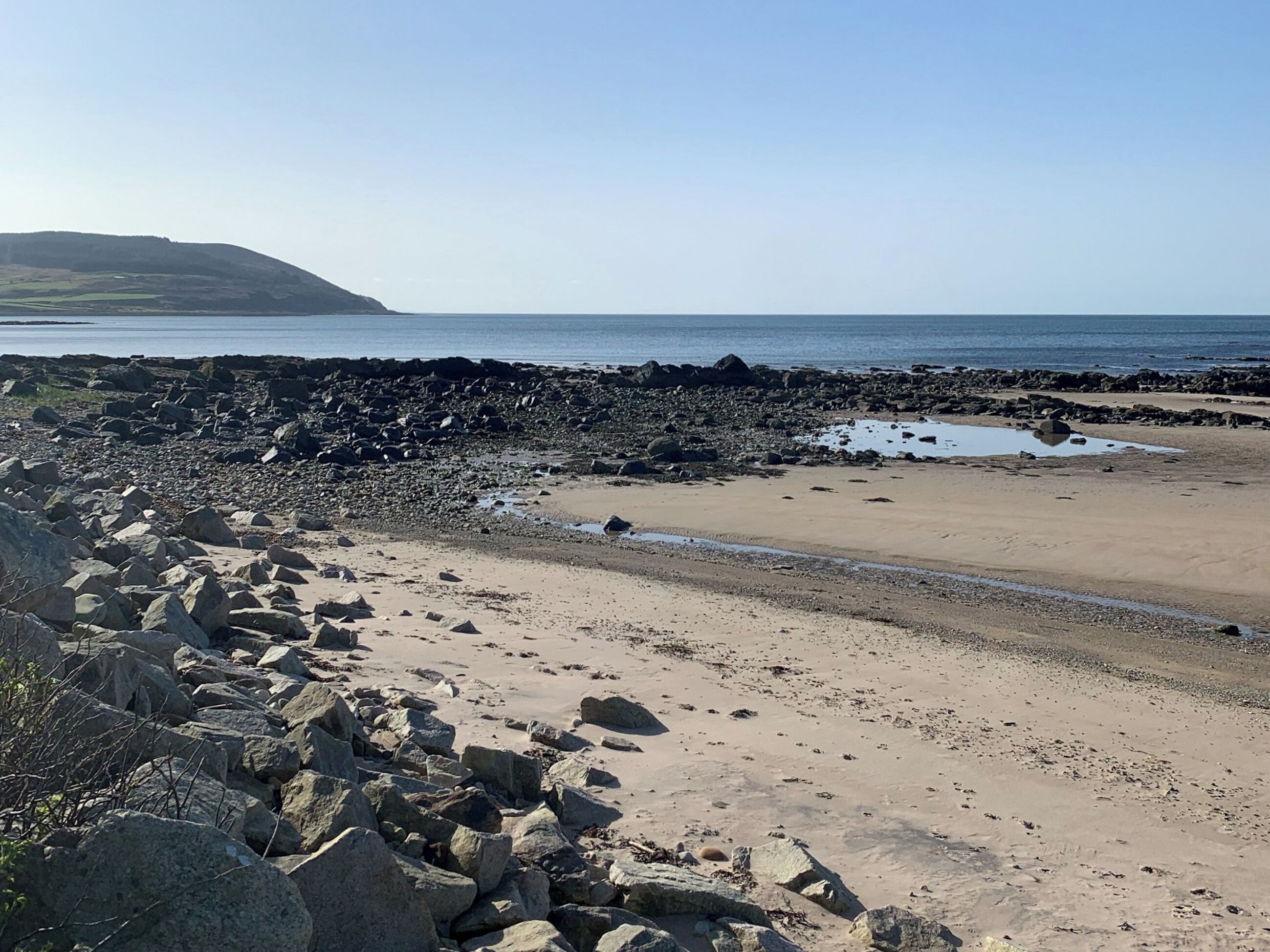 Une plage rocheuse offrant une vue dégagée sur l’océan et une colline lointaine.
