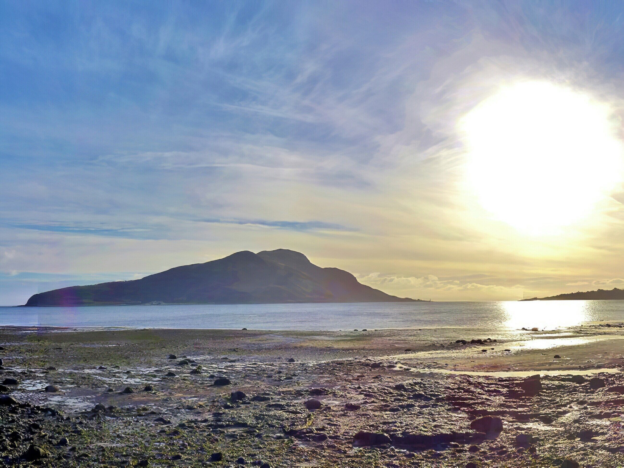 A beach with a mountain in the background, rocky shore, and calm sea.