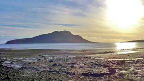 Une plage avec une montagne en arrière-plan, un rivage rocheux et une mer calme.