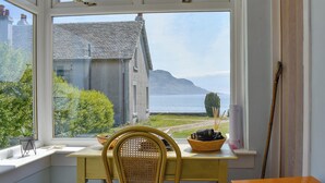 Une pièce avec vue sur un bâtiment et sur l’eau, une table avec une chaise, et une fenêtre avec un rideau.