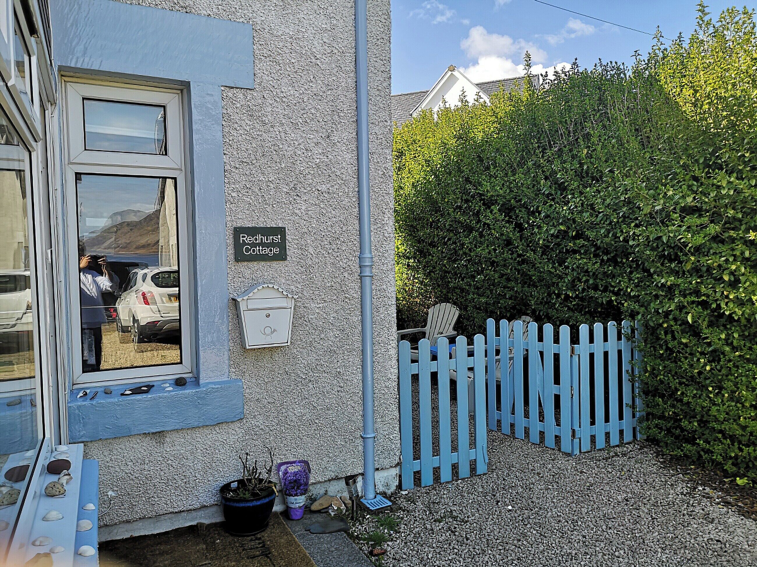 A cottage named 'Redhurst Cottage' with a blue exterior, a white mailbox, and a wooden fence.