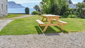 Une table de pique-nique se trouve dans un espace herbeux, et un chemin de gravier mène à une maison.