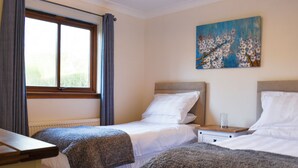 A bedroom with two beds, a window with curtains, a painting on the wall, and a bedside table with a glass. - 3 bedroom accommodation in Lamlash (Lamlash)