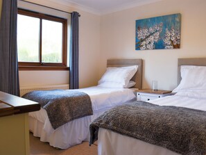 A bedroom with two beds, a window with curtains, a painting on the wall, and a bedside table with a glass. - 3 bedroom accommodation in Lamlash (Lamlash)