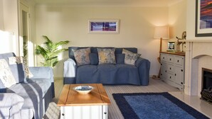 A living room with a sofa, a coffee table, a lamp, a fireplace, and a framed picture on the wall. - 3 bedroom accommodation in Lamlash (Lamlash)