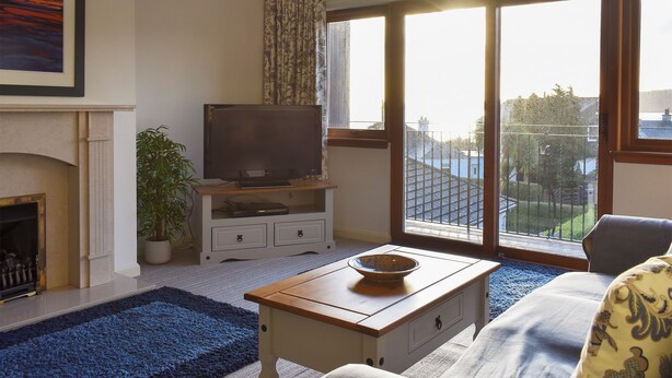 A living room with a fireplace, a television on a stand, a coffee table, and a view through large windows. - 3 bedroom accommodation in Lamlash (Lamlash)