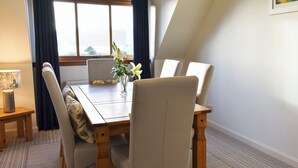 A dining area with a wooden table, six chairs, a vase with flowers, and a lamp on a side table. - 3 bedroom accommodation in Lamlash (Lamlash)