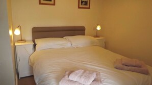 A neatly made bed with white linens and two pillows, flanked by bedside tables with lamps. There are two framed pictures on the wall above the bed. - A real ’Escape to the Country’ in truly welcoming surroundings. (Askrigg)