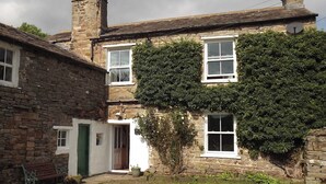 A stone building with a green door, a bench, and a small garden area. - A real ’Escape to the Country’ in truly welcoming surroundings. (Askrigg)