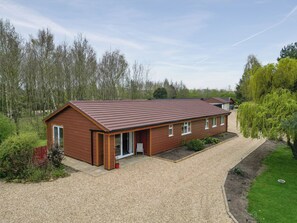 A single-story wooden building with a sloped roof, a gravel driveway, and a surrounding garden.