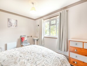 Ein Schlafzimmer mit einem Bett, einem Nachttisch, einer Kommode, einem Fenster mit Vorhängen, einem Wandspiegel und einem Bild.