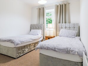 Quarto com duas camas, cada uma com cabeceira, mesa de cabeceira e janela com cortinas.