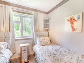 Um quarto com cama, mesa de cabeceira, janela com cortinas, prateleira e um quadro de girafa na parede.