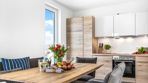 A modern kitchen with wooden cabinets, a dining area with a wooden table, and a view of the sky through a window. - Beach front apartment in Olpenitz (Olpenitz)