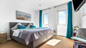 A modern bedroom with a bed, a side table, a chair, and a window with curtains. - Beach front apartment in Olpenitz (Olpenitz)