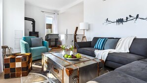 A modern living room with a sofa, a teal armchair, a vintage suitcase coffee table, and a fireplace. - Beach front apartment in Olpenitz (Olpenitz)