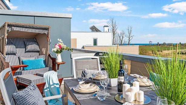 A rooftop dining area with a table set for four, surrounded by wicker furniture and a view of the sea. - Beach front apartment in Olpenitz (Olpenitz)