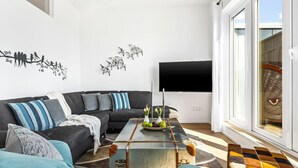 A modern living room with a black sectional sofa, a coffee table with fruit, and a flat-screen TV mounted on the wall. - Beach front apartment in Olpenitz (Olpenitz)