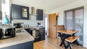 A modern kitchen with dark cabinets, a wooden dining table, and a large window with blinds.